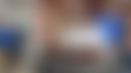 Four people hold a large check for $25,000 at Dave Hahler Automotive. The setting is indoors, with balloons and food in the background.