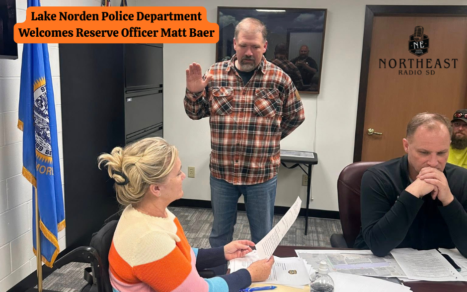 Man in plaid shirt taking an oath, hand raised. Woman seated holding paper. Blue flag visible. Office setting with Northeast Radio logo.