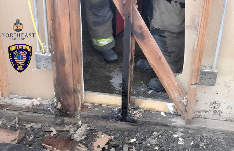 Fire-damaged doorway with charred wood and debris; firefighters stand inside. Northeast Radio SD and Watertown Fire Rescue logos visible.