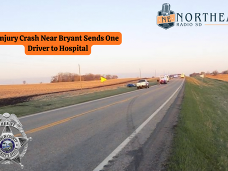 Rural road scene with emergency vehicles at sunset. Text reads "Injury Crash Near Bryant Sends One Driver to Hospital." Sheriff's badge logo.