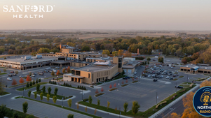 Aerial view of Sanford Health building at sunset, with parking lot and green landscape. Logos for Sanford Health and Northeast Radio SD.