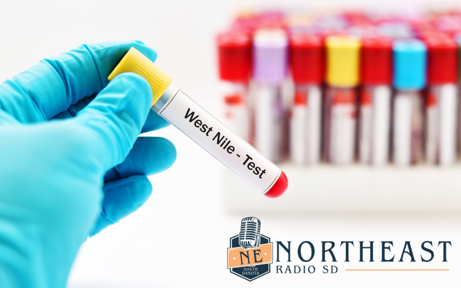 Gloved hand holds a test tube labeled West Nile - Test, with blurred colorful sample tubes and Northeast Radio SD logo.