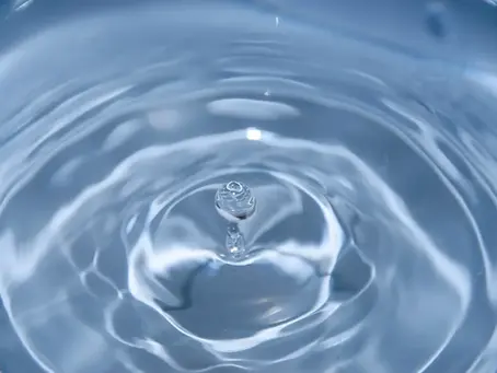 Water droplet splashing upwards, creating ripples on a smooth, reflective surface. Soft blue hues, serene and fluid motion.