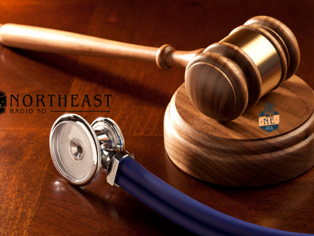 Wooden judge’s gavel beside a blue stethoscope on a polished desk, with Northeast Radio SD logos, suggesting legal-medical news.