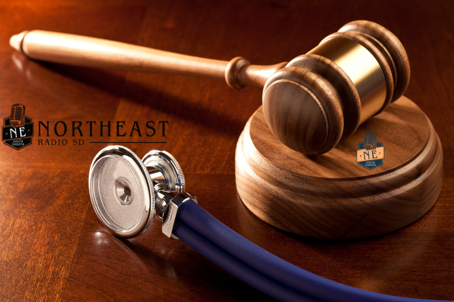 Wooden judge’s gavel beside a blue stethoscope on a polished desk, with Northeast Radio SD logos, suggesting legal-medical news.