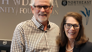 Smiling man and woman pose in a radio studio with North East Radio SD and foundation logos.