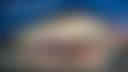 Gas station at dusk with bright lights, red pumps, and a car. Text reads: Watertown to review zoning for gas stations in industrial areas. Logos present.