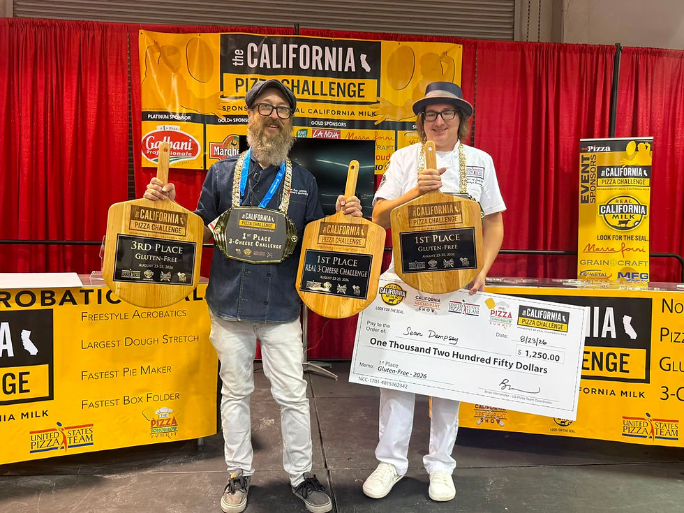Two men at California Pizza Challenge hold prize paddles and a $1,250 check on a red-curtained stage, smiling.