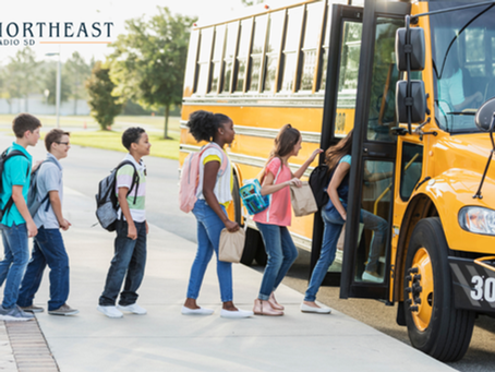 Students with backpacks line up to board a yellow school bus outside, with NORTHEAST RADIO SD logo visible on the image.