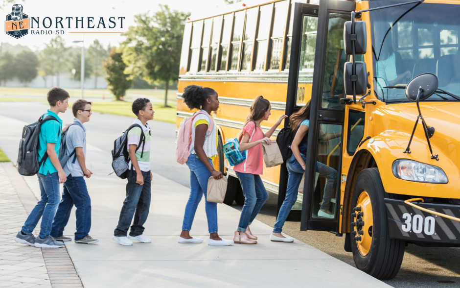 Students with backpacks line up to board a yellow school bus outside, with NORTHEAST RADIO SD logo visible on the image.
