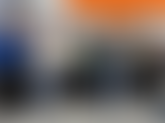 Group of 14 people smiling indoors, standing in front of a wall with logos and text about a retailer's association cohort. Casual attire.