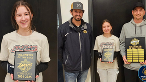 Young woman holding a "Volunteer of the Year" plaque, smiling with two men. Wearing casual clothes, indoors, with awards featuring Lakers logo.