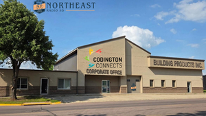 Commercial building with Coddington Connects and Building Products Inc. signs under a blue sky, with a tree at left.