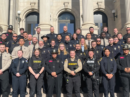 A group of uniformed officers posing on courthouse steps, with insignias and badges visible. Emblems displaying South Dakota and a radio logo.