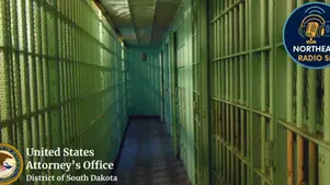 Dimly lit green prison corridor with metal bars. Text: "United States Attorney’s Office, District of South Dakota," "Northeast Radio SD" emblem.