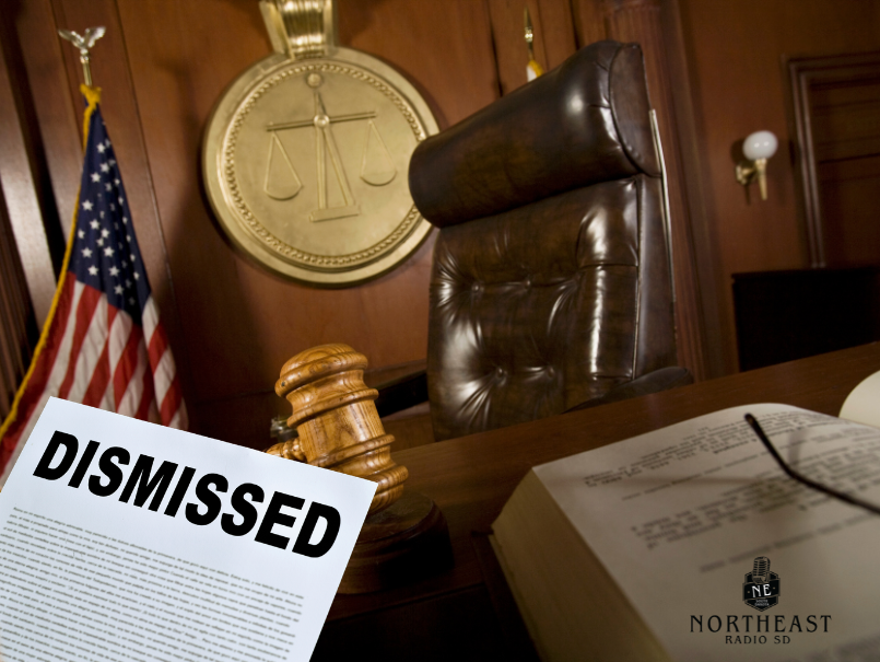 Empty courtroom with judge’s chair, gavel and U.S. flag; a document marked DISMISSED lies on the desk.