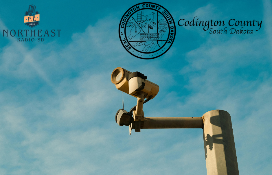 Security camera on a pole against blue sky, with Northeast Radio SD and Codington County South Dakota logos and text.