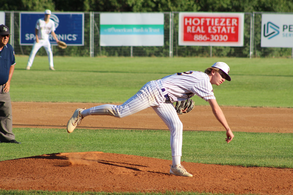 Baseball pitcher in white pinstripes throws from the mound on a sunny field, with outfield ads and an umpire nearby.