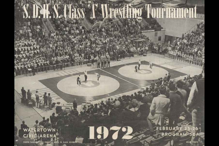 Packed arena wrestling tournament with two matches on mats; large crowd. Text reads S.D.H.S. Class A Wrestling Tournament, 1972.