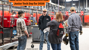 People in a workshop discuss tech day plans. Red equipment in the background. Text: Lake Area Tech Announces Final Junior Tech Day for 2026.