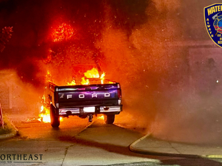 Ford pickup engulfed in flames and smoke on a street at night, with Watertown Fire Rescue and Northeast Radio SD logos visible.