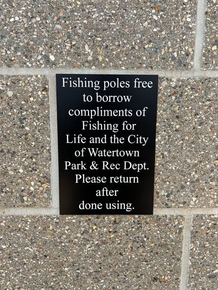 Black sign on speckled brick wall reads fishing poles free to borrow; return after use.