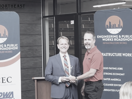 Two men shake hands at an Engineering & Public Works Roadshow, with a banner reading Infrastructure Works behind them.