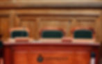 Empty wood-paneled hearing room with three green chairs and microphones; podium reads NORTHEAST RADIO SD, calm and formal.