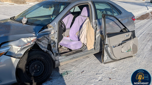 Damaged silver car with open door and purple seats on snowy street. Front left side heavily dented. "NORTHEAST RADIO SD" logo visible.