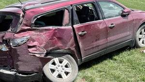 Damaged maroon SUV in a grassy yard after a crash, with a tow truck and people in the background; Northeast Radio SD logo visible.