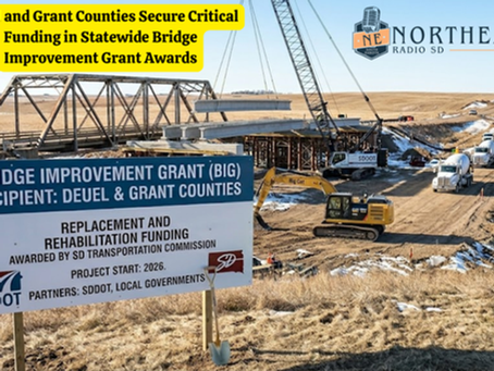 Construction site with a bridge under repair, cranes, and machinery. Sign details grant awards for Deuel and Grant Counties. Rural background.