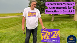 Man in a white shirt holding a hammer, standing on a grassy lawn next to a campaign sign reading "Glen Vilhauer for State Senate."