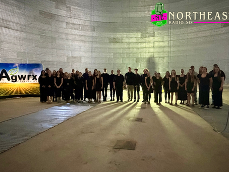 Group of people in black pose inside a large grain silo beside an Agwrx Cooperative sign and Northeast Radio SD logo.