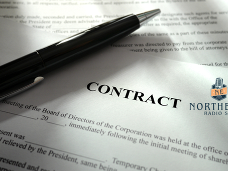Black pen lies on a contract document with Northeast Radio SD logo, lit by soft light.