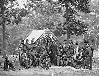 black and white photograph of Civil War soldiers standing in a group at camp
