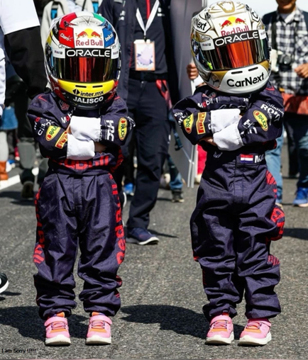 Two children wearing race suits and helmets.