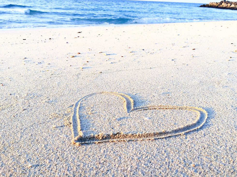 A photo of the beach with a blue filter, in the sand is drawn a heart.