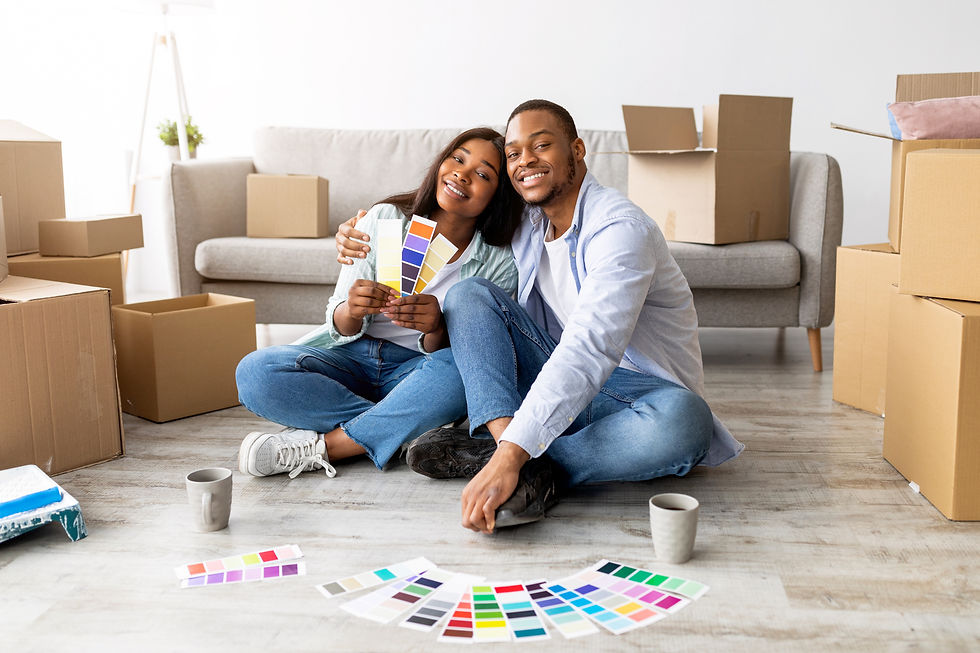 Smiling African American couple sitting on the floor surrounded by moving boxes, holding color swatches while planning renovations for their new home. A cozy and joyful moment symbolizing fresh beginnings.
