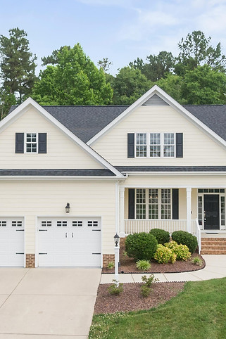 Front view of a charming single-family home with a well-maintained lawn, two-car garage, and inviting front porch, surrounded by lush greenery, representing a dream home for potential buyers.