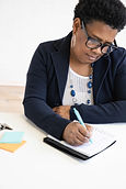 A focused black woman in professional attire takes notes diligently, symbolizing leadership development, business strategy planning, and the targeted personal growth services offered by Sonya's life coaching brand.