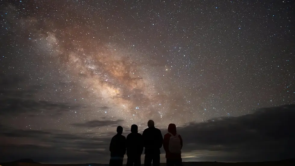 Fire mennesker ser op mod en stjerneklar nattehimmel og Mælkevejen i et billede til indlægget om, hvordan begyndte universet.