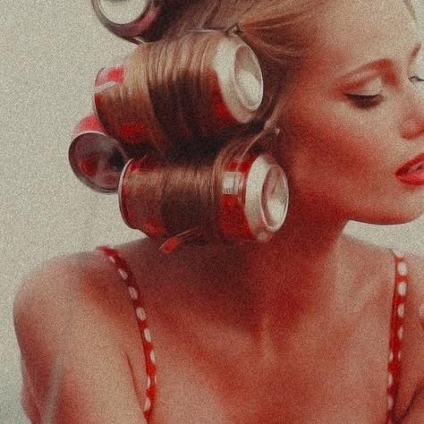 Young woman with Coke can rollers, red lipstick, and polka dot straps applies nail polish. Relaxing mood with a neutral background.