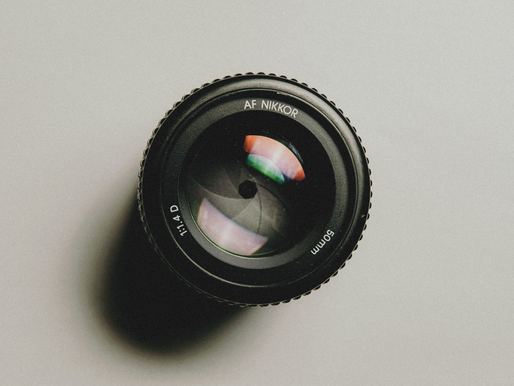 Camera lens labeled "AF NIKKOR 50mm f/1.4D" on a light gray background, showcasing colorful lens reflections.
