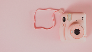 Pink instant camera with strap on a pale pink background, creating a soft, minimalist mood