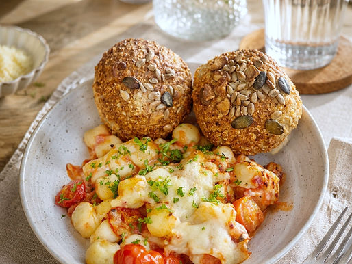 Überbackene Gnocchi mit cremiger Tomatensauce, veganem Bacon und geschmolzenem Käse in einer Auflaufform, serviert mit frisch gebackenen Hüttenkäse-Semmeln aus dem Airfryer.  