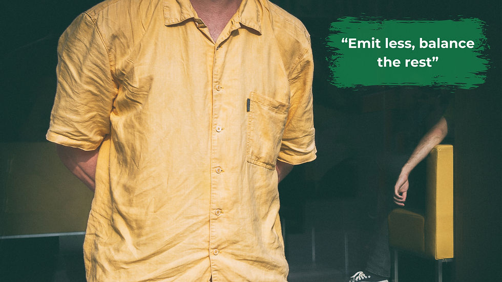 A man is standing with a yellow shirt on in a dark room and there is a person behind him