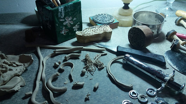 Pequenos pedaços de barro saídos e uma extrusora, faca, cortadores, carimbos, um portalápis em cima de uma mesa iuminads por um abajour.