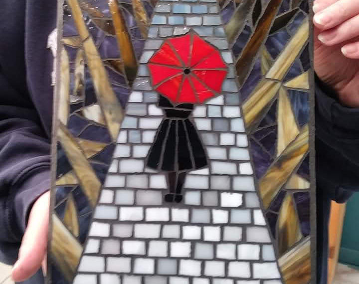 Photo of a workshop student holding up their completed mosaic creation.