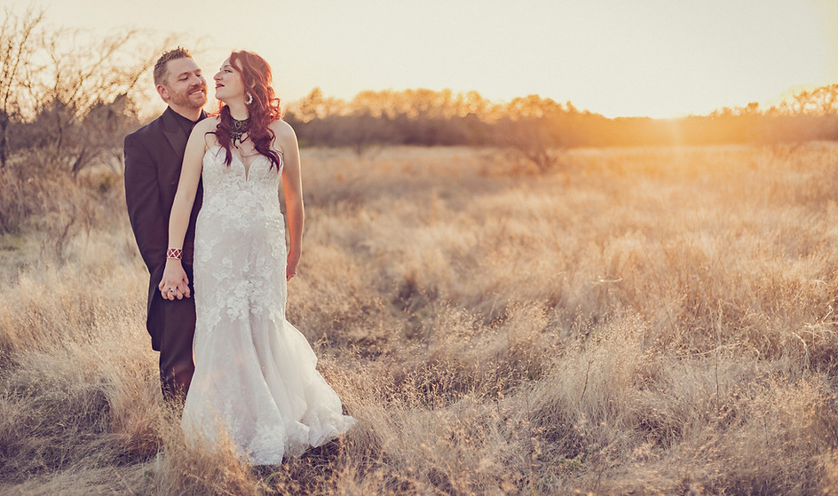 A redheaded bride and her groom embrace in a field of tall grass