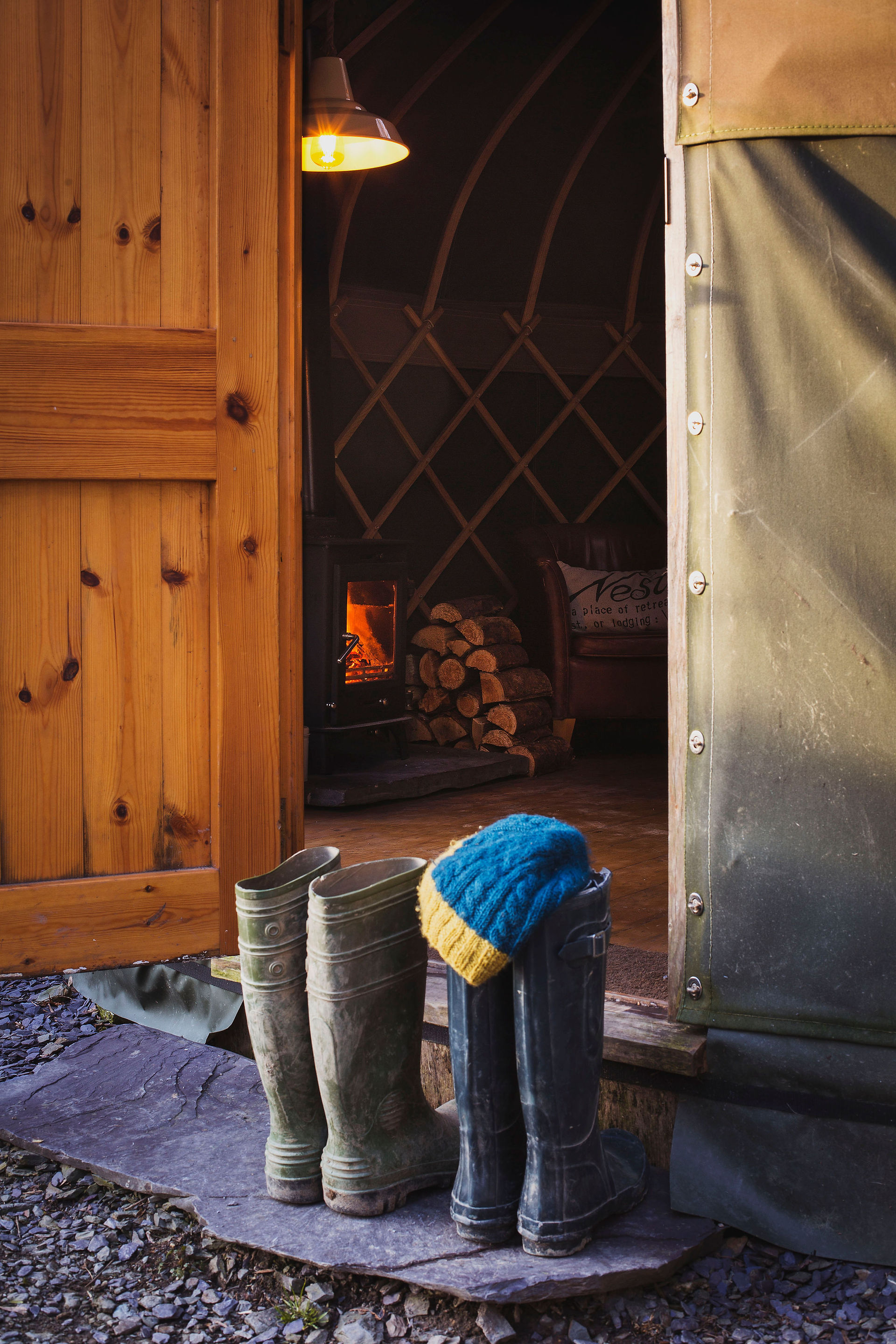 Glamping yurt with tow pairs of wellies outside, you can see the fire lit inside